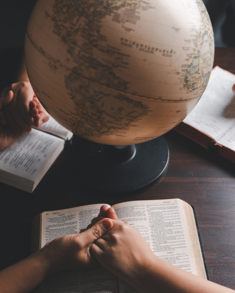 Mains jointes devant une Bible et un globe terrestre