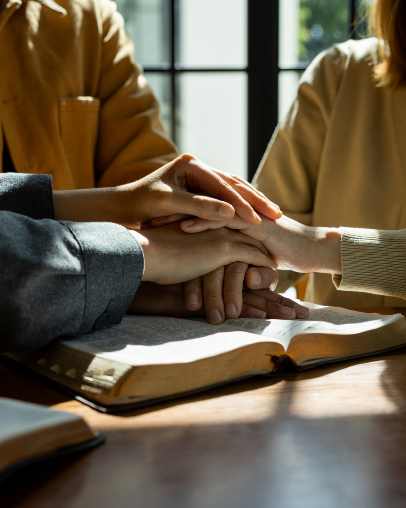Des personnes posent leurs mains ensemble au-dessus d’une Bible ouverte
